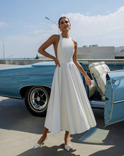 Woman in a white dress standing next to a vintage blue car on a sunny day.