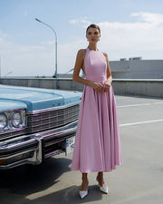 Woman in a pink dress standing next to a vintage car on a road.