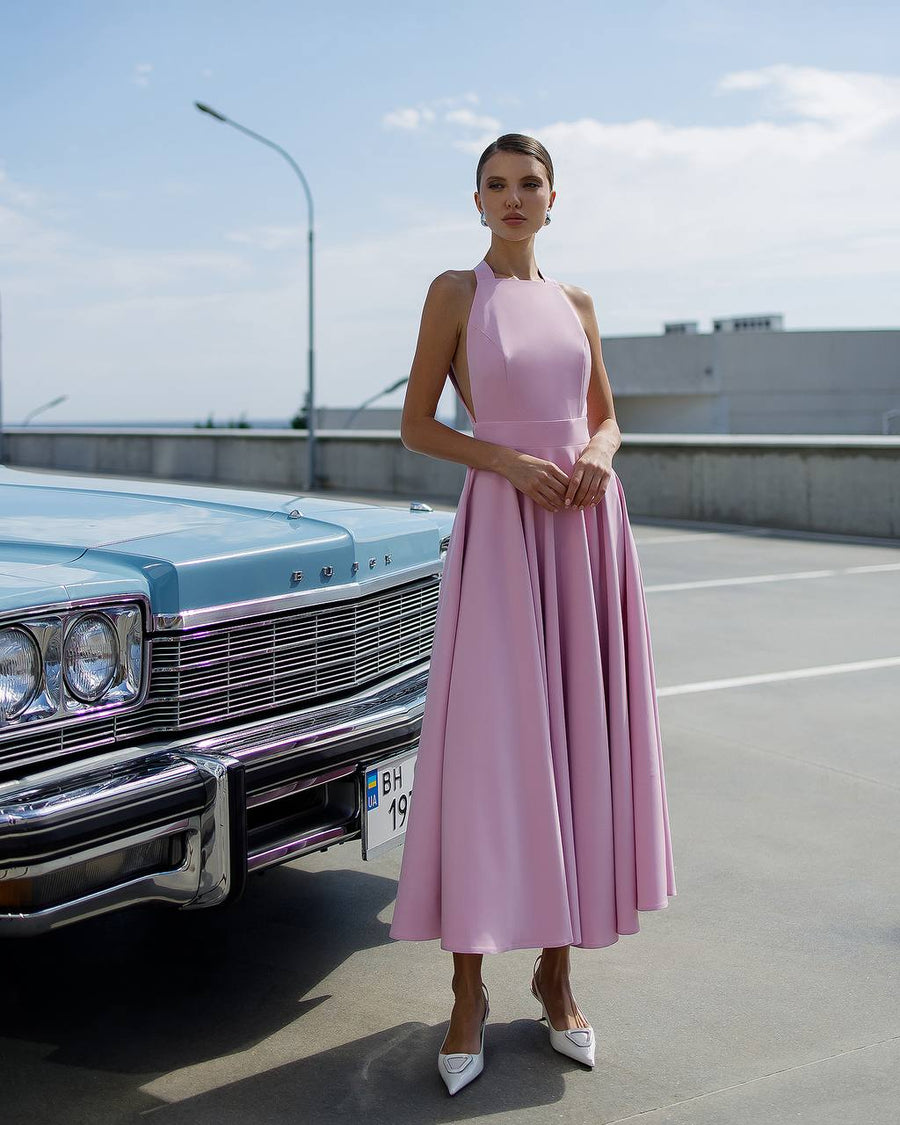 Woman in a pink dress standing next to a vintage car on a road.