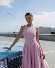 Woman in a pink dress standing next to a vintage car on a clear day.
