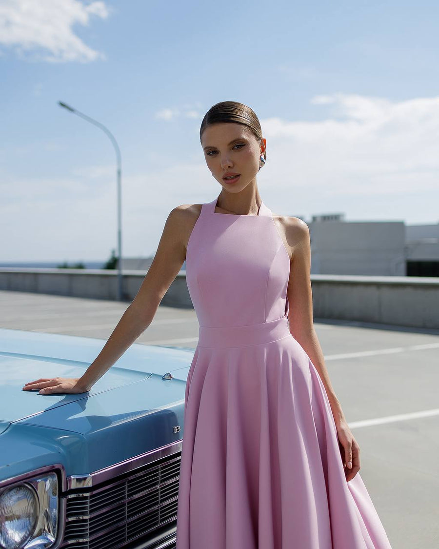 Woman in a pink dress standing next to a vintage car on a clear day.