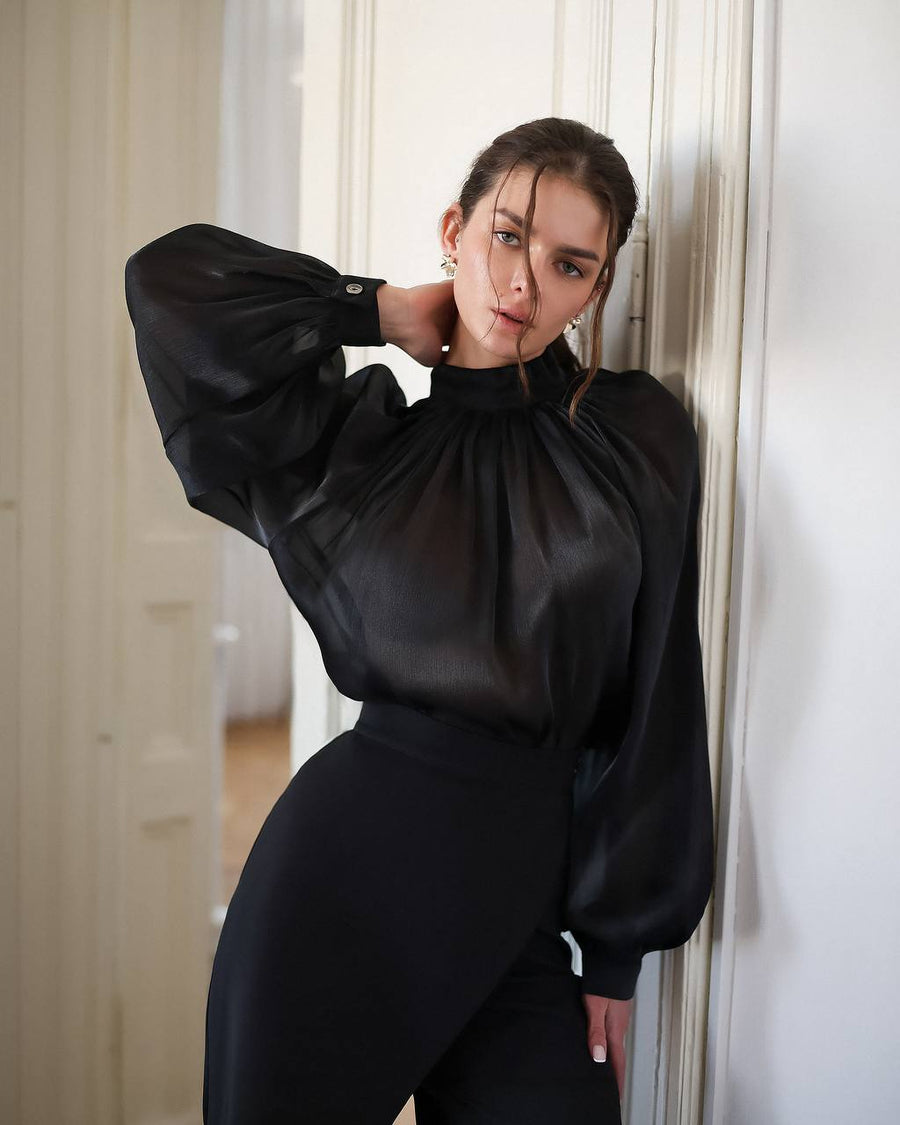 Woman wearing a black outfit leaning against a white wall.