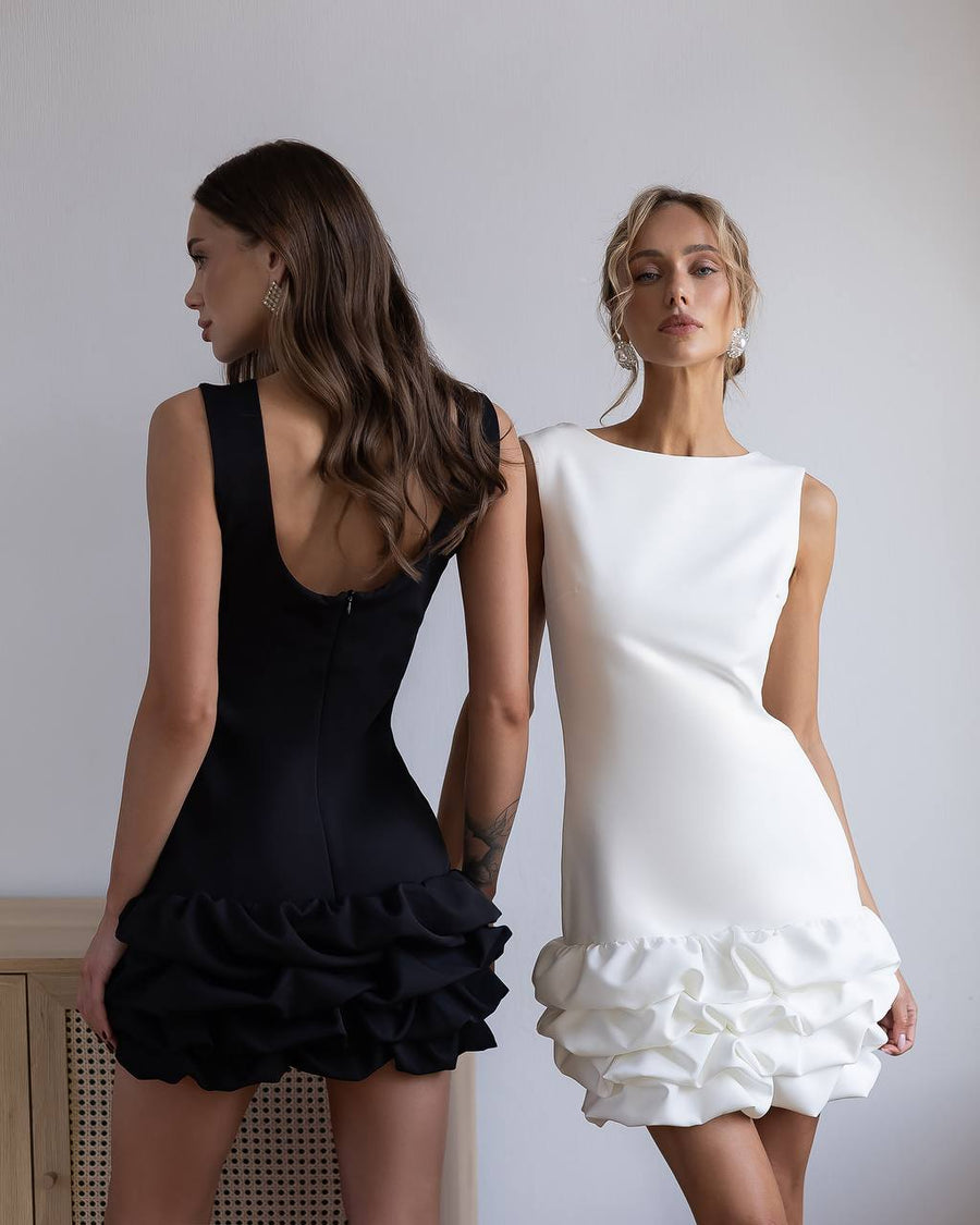 Two women wearing black and white ruffled dresses against a plain background