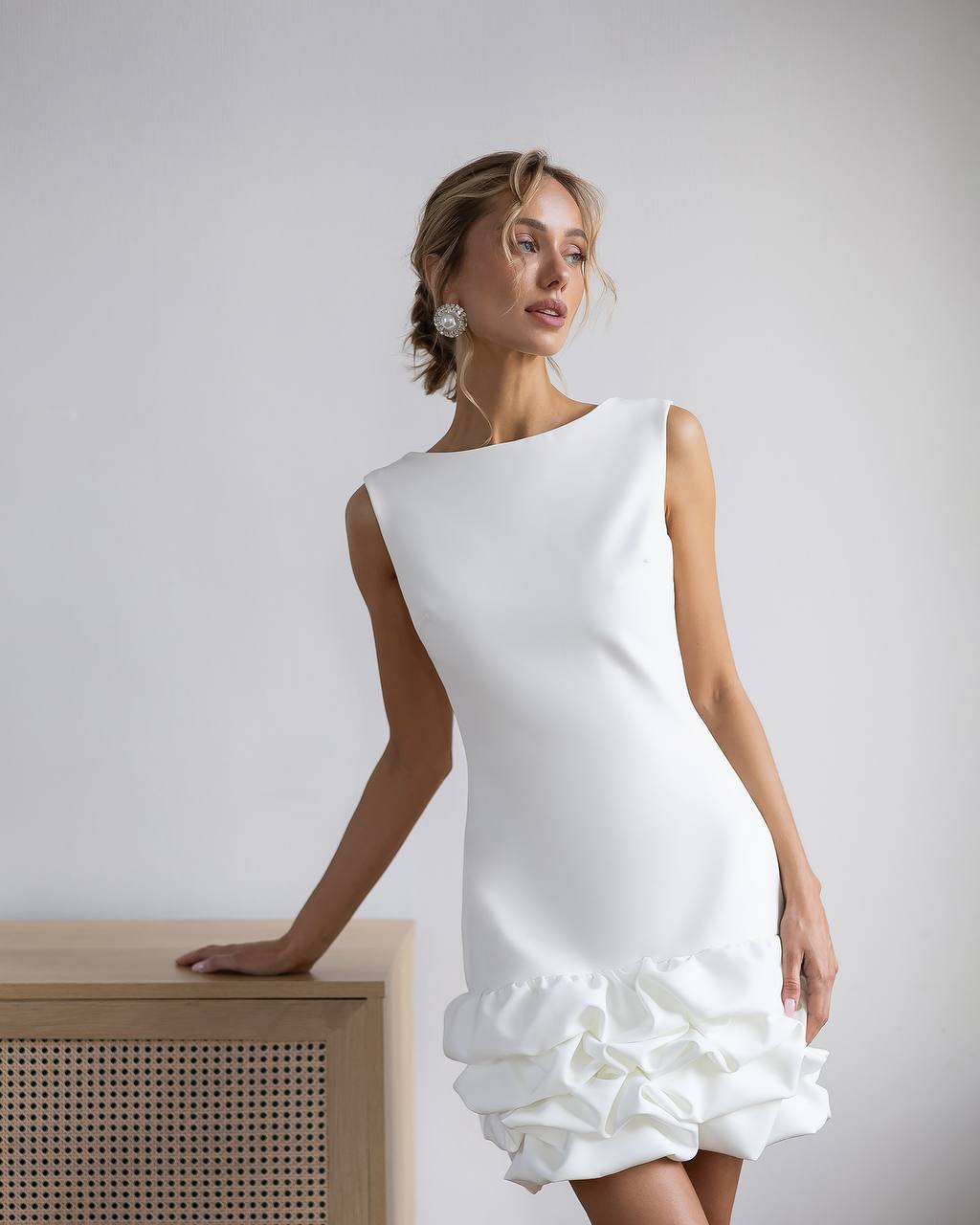 Woman wearing a white dress with ruffled bottom half against a plain background