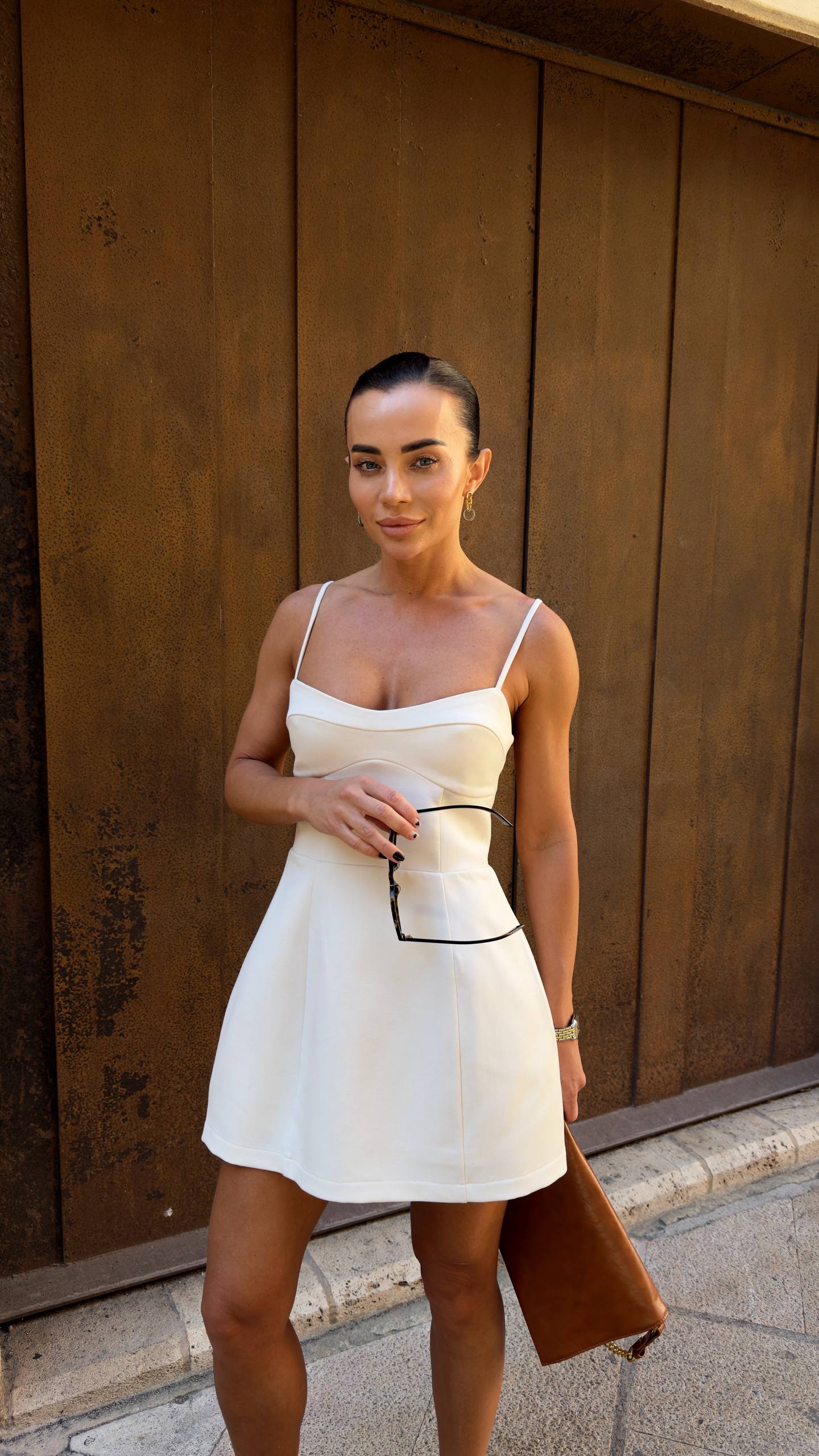 Woman in a white dress standing against a wooden wall.