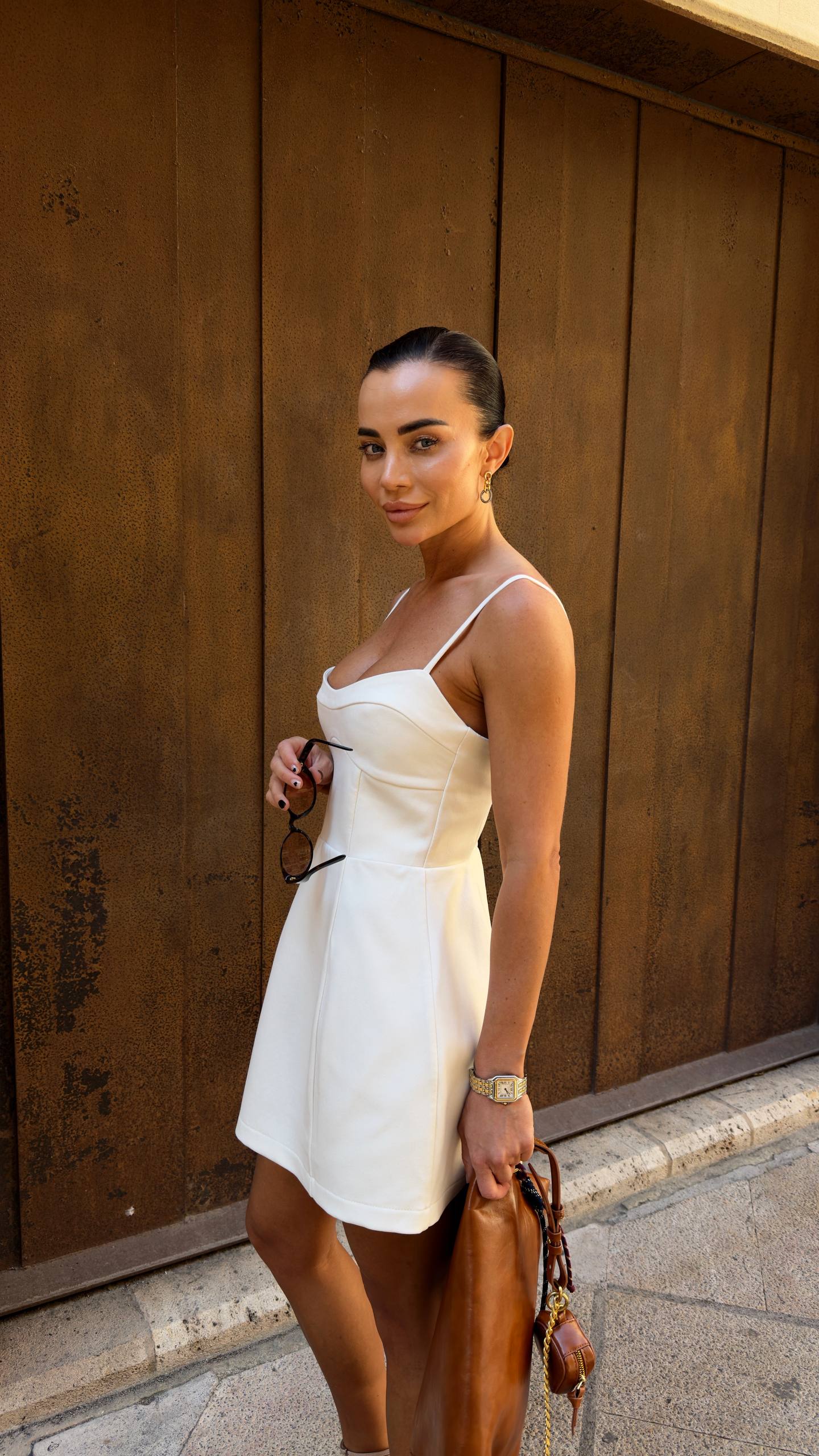 Woman in a white dress standing against a wooden wall.