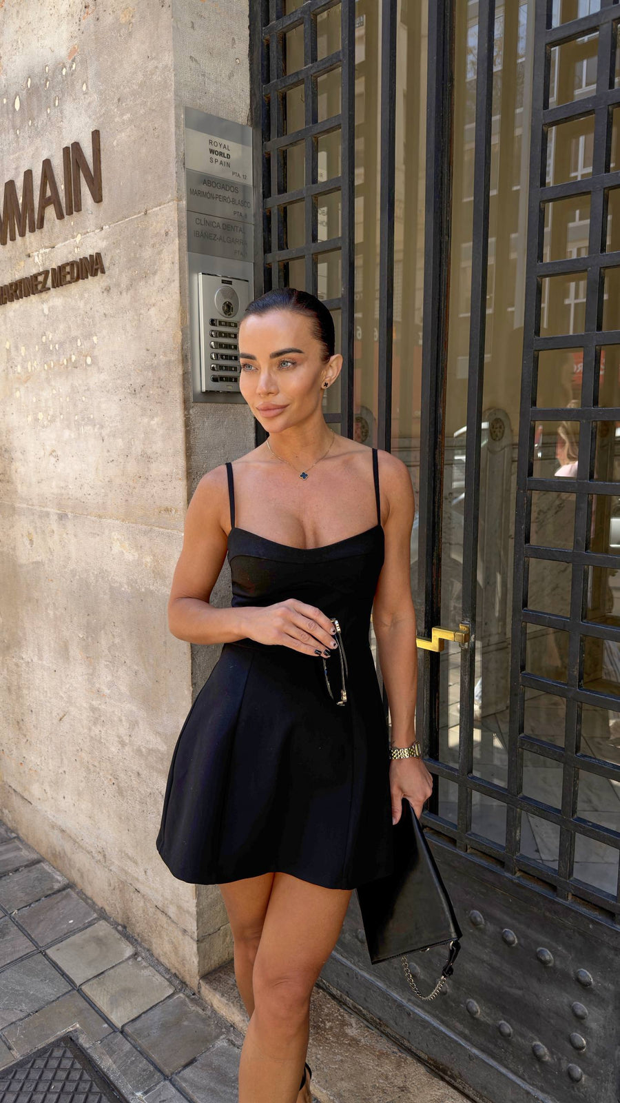 Woman in a black dress standing outside a building with a glass door.