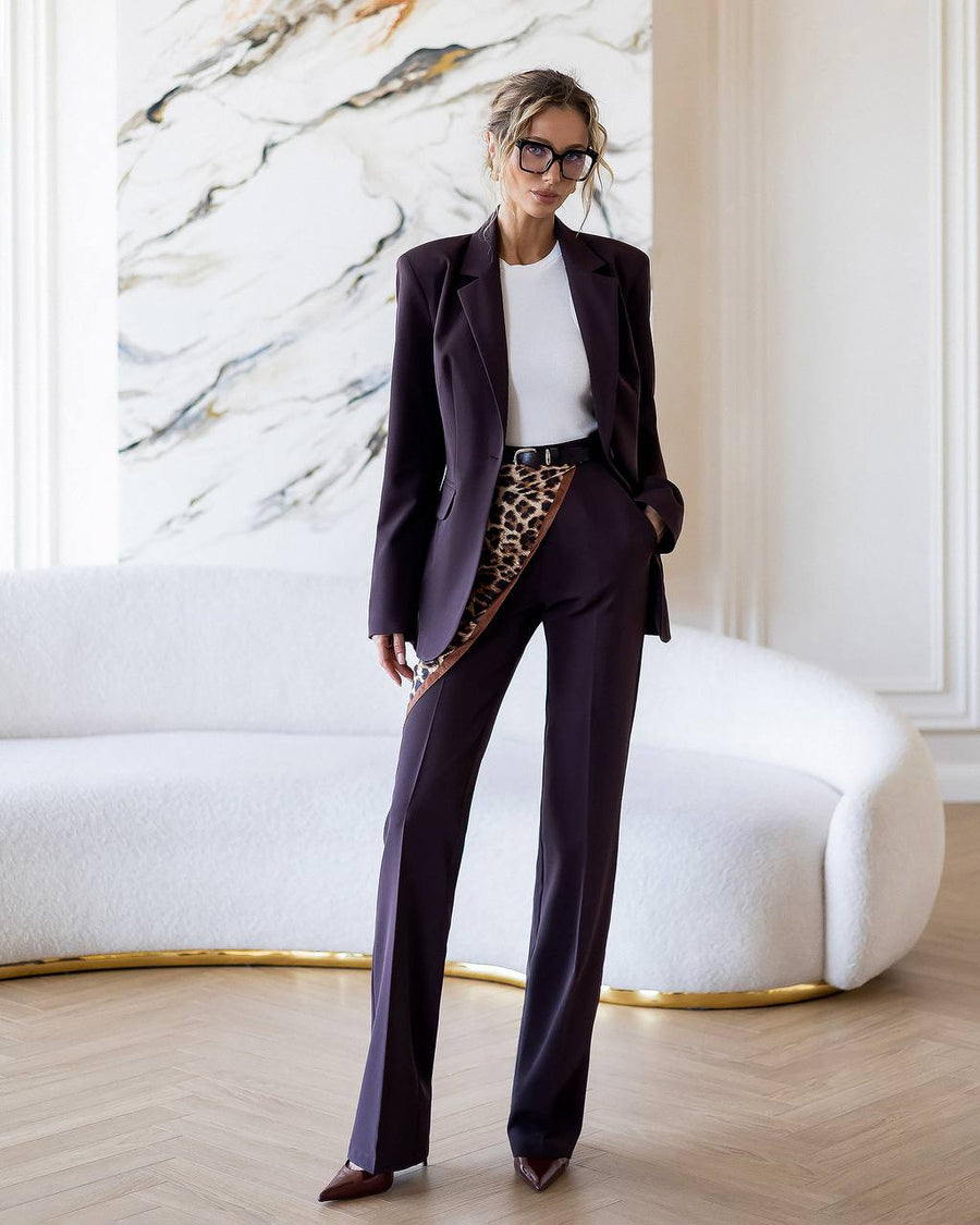 Woman in a dark suit with a white shirt and leopard print belt in a stylish room.