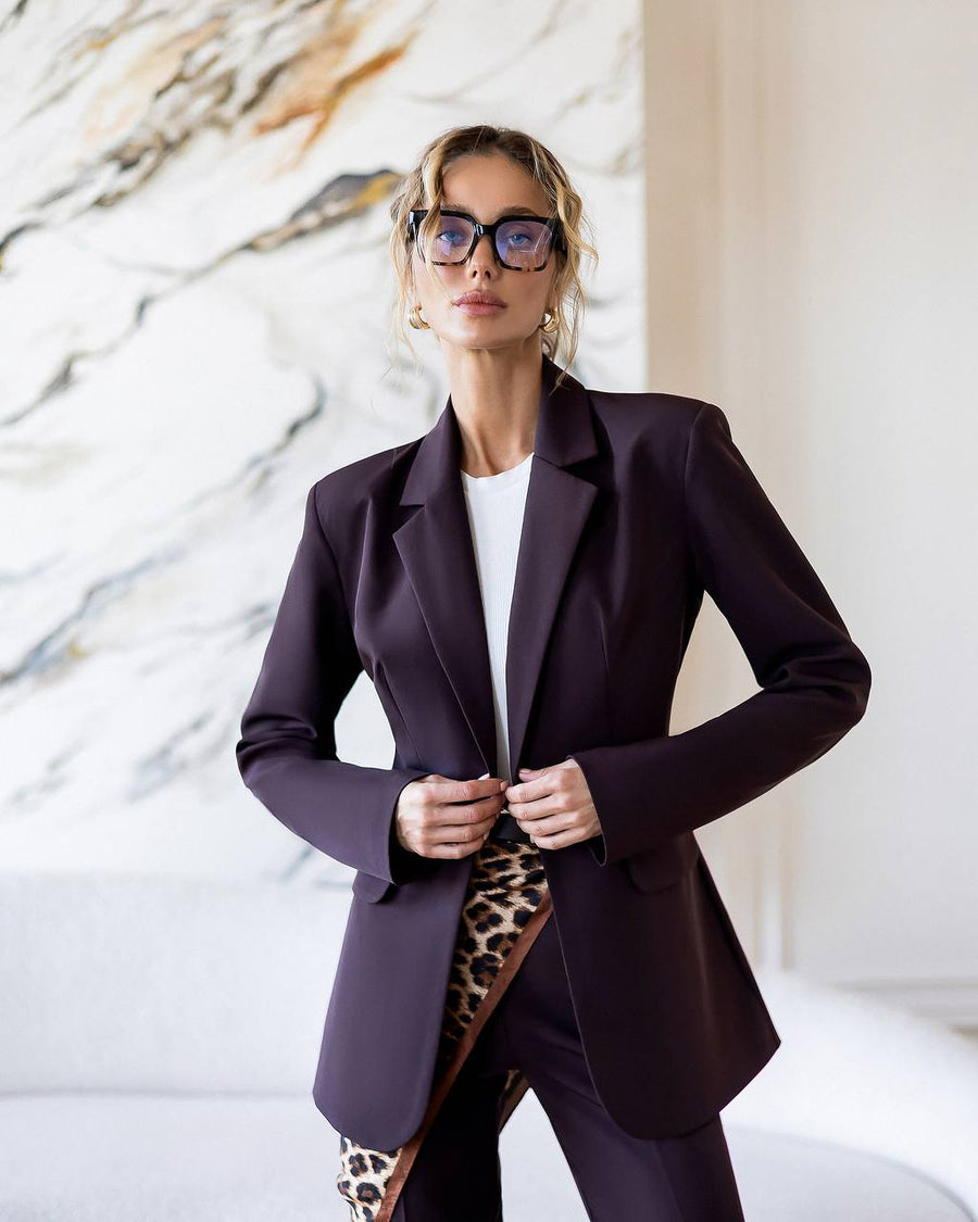 Woman wearing a dark purple blazer and leopard print skirt against a marble wall.