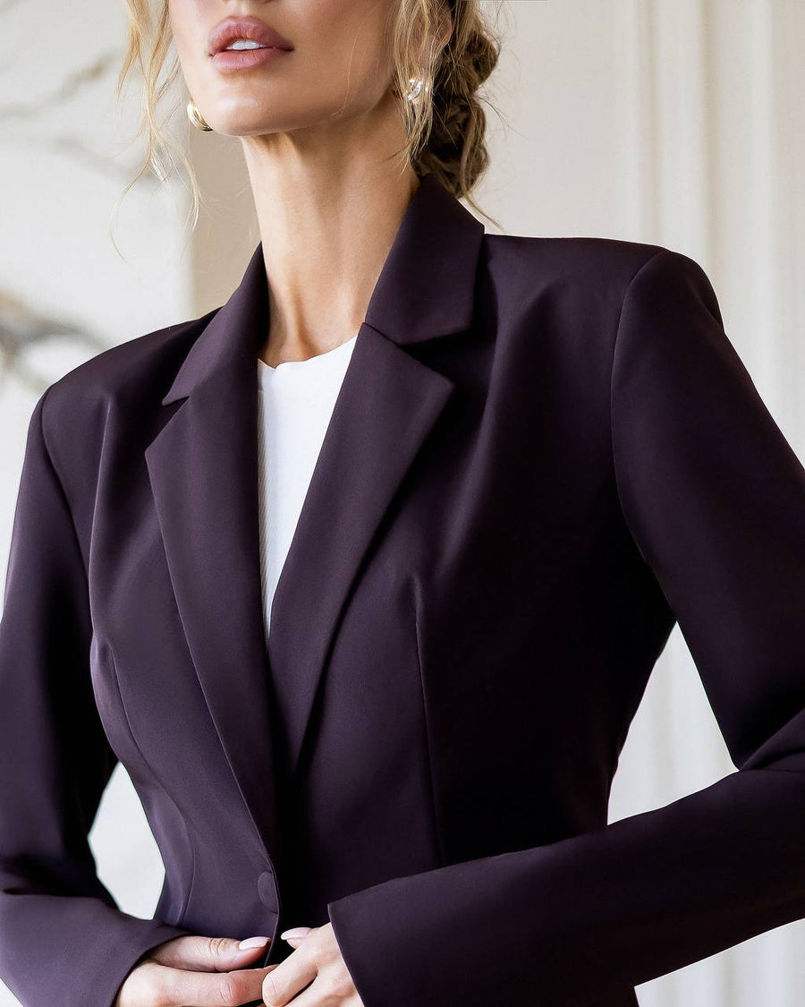 Woman wearing a dark purple blazer over a white top against a neutral background