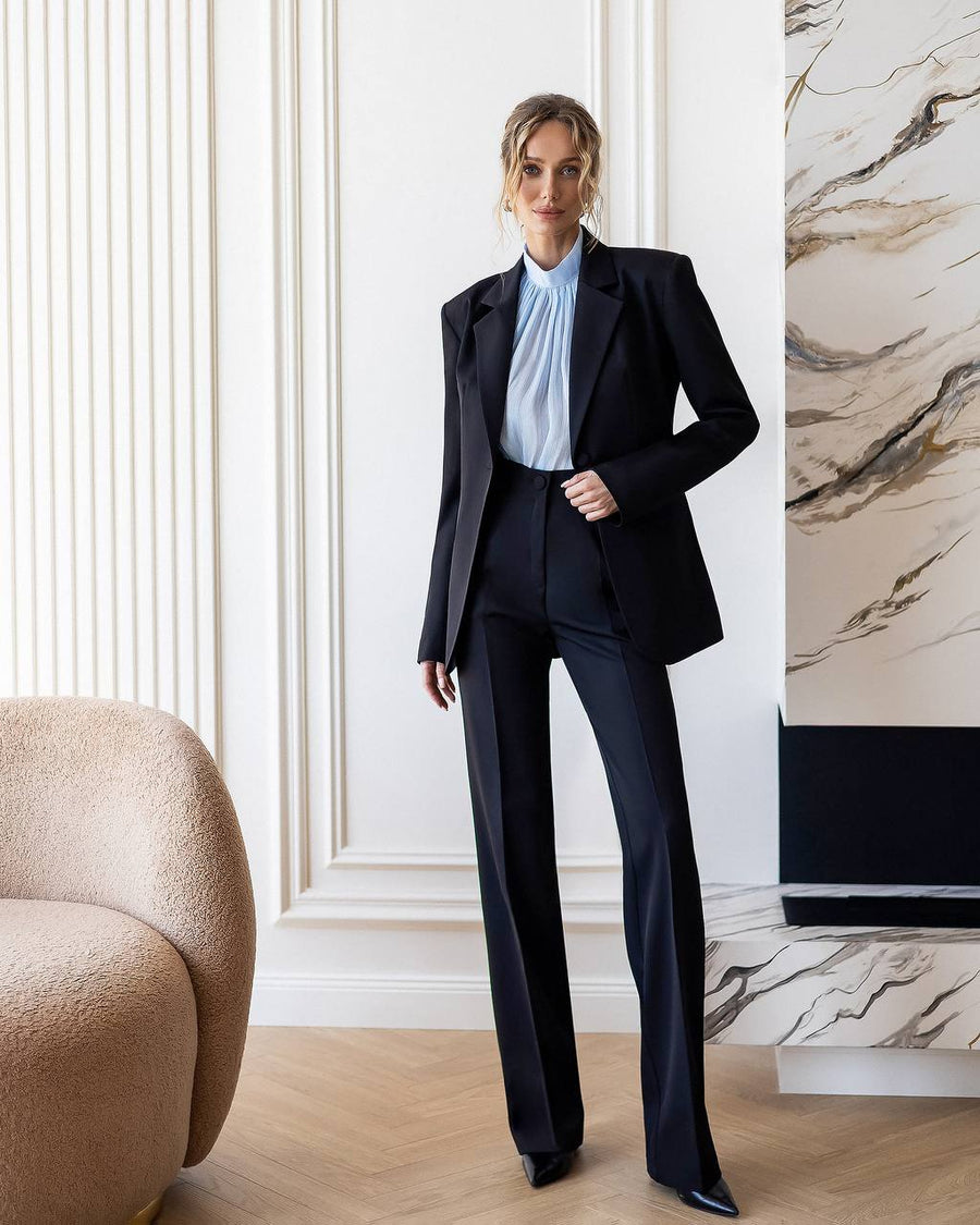 Woman in a black suit standing in a stylish room with marble wall.