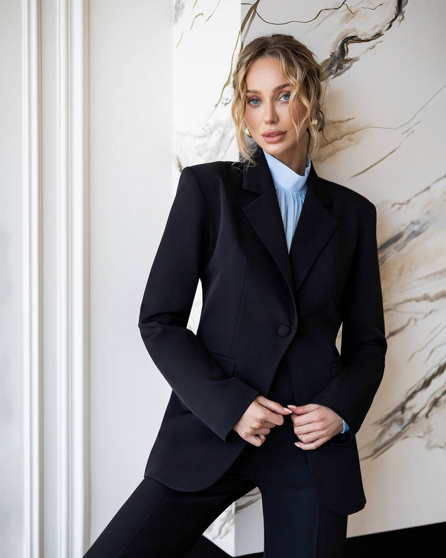 Woman wearing a black suit against a marble wall