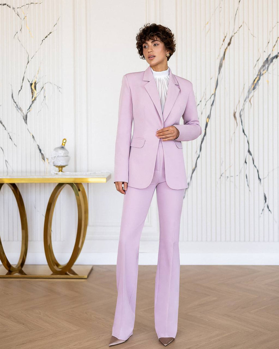 Woman wearing a light purple suit standing in a room with marble walls and a gold table.