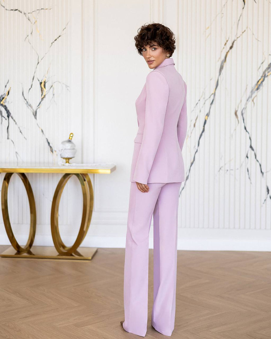 Woman in a lavender suit standing in a stylish room with marble walls and a gold table.