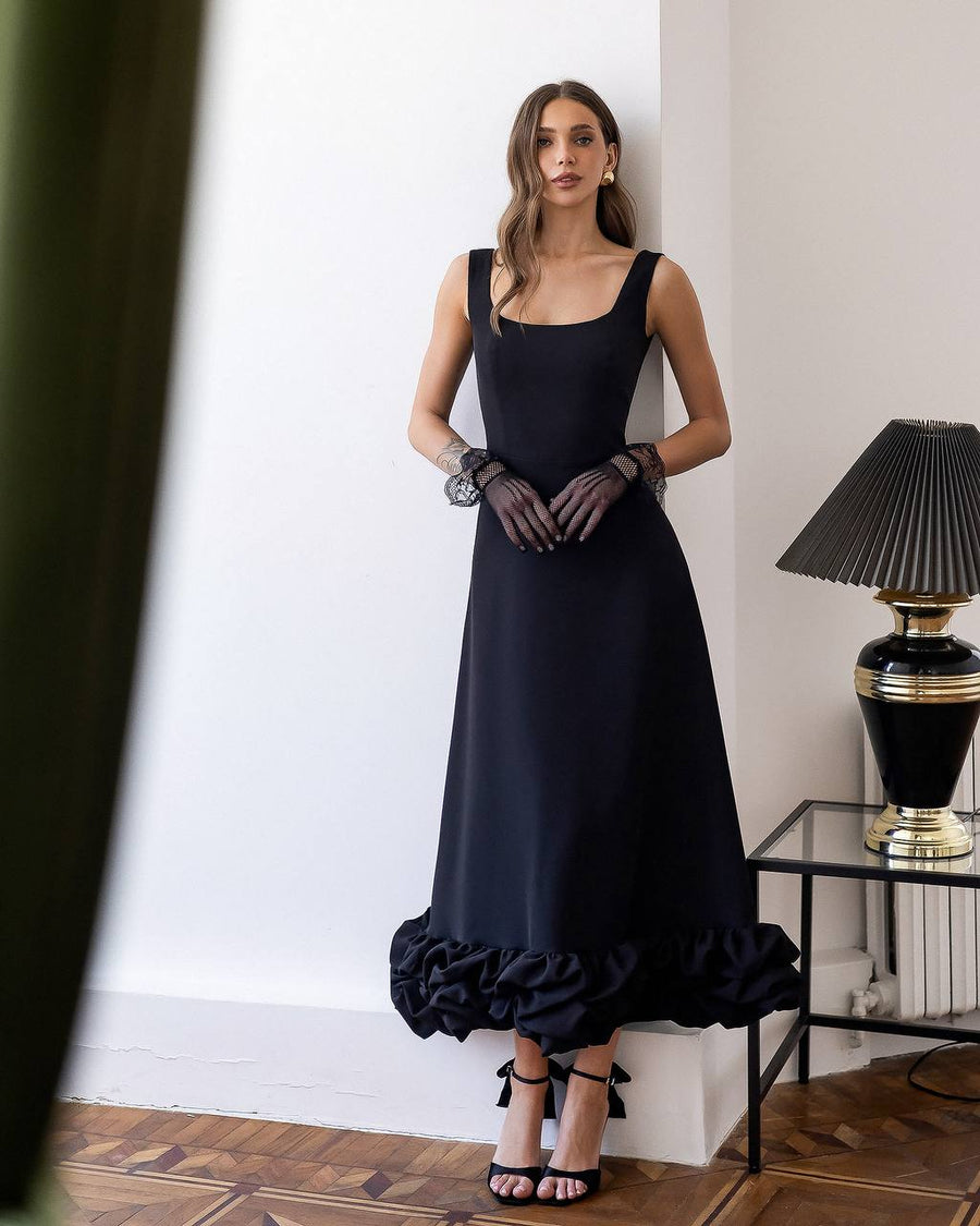 Woman wearing a black dress with ruffled hem in an elegant room.
