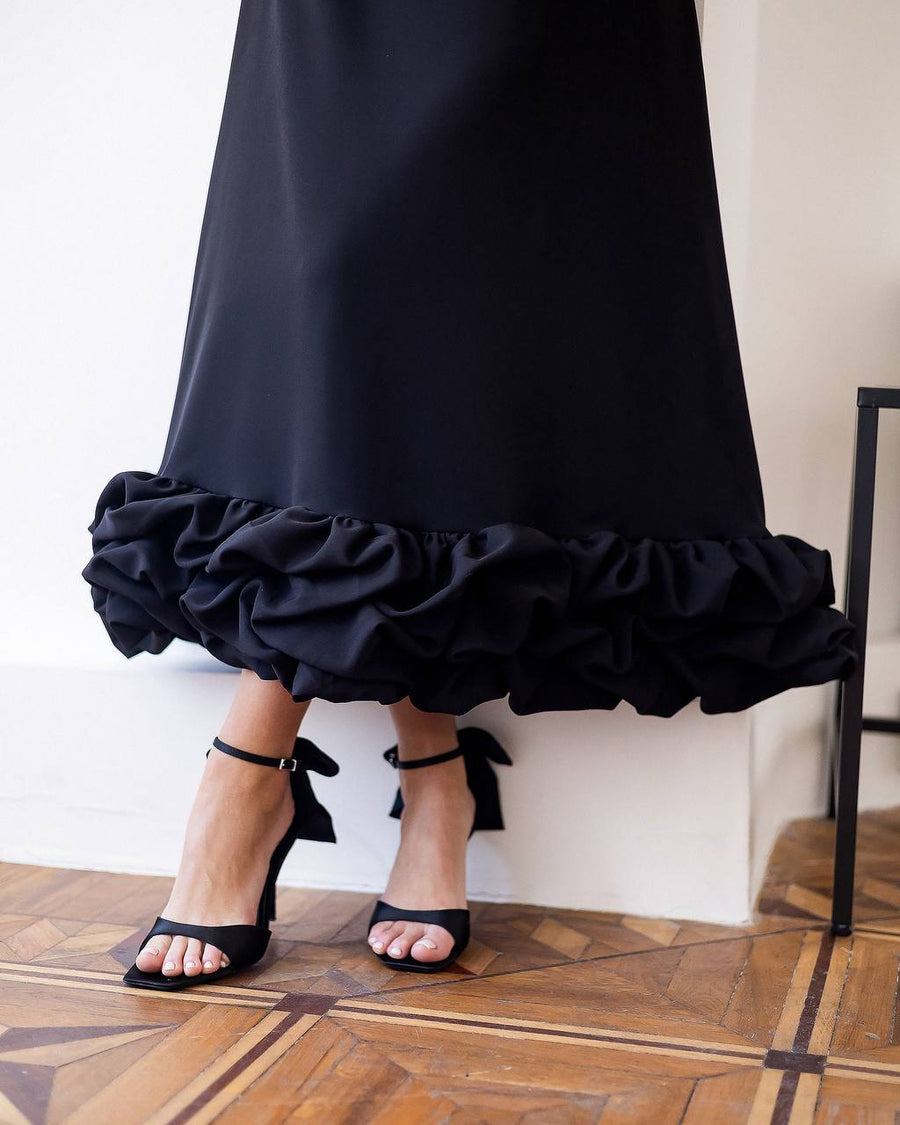 Black ruffled skirt worn by a person on a wooden floor.