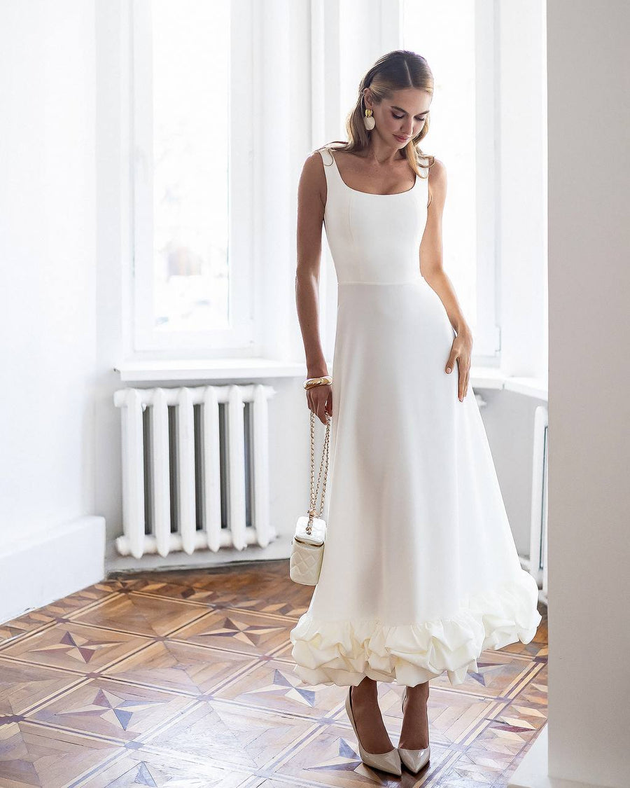 Woman in a white dress standing in a room with tiled floor and white walls.