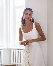 Woman in a white dress standing in a bright room with large windows.