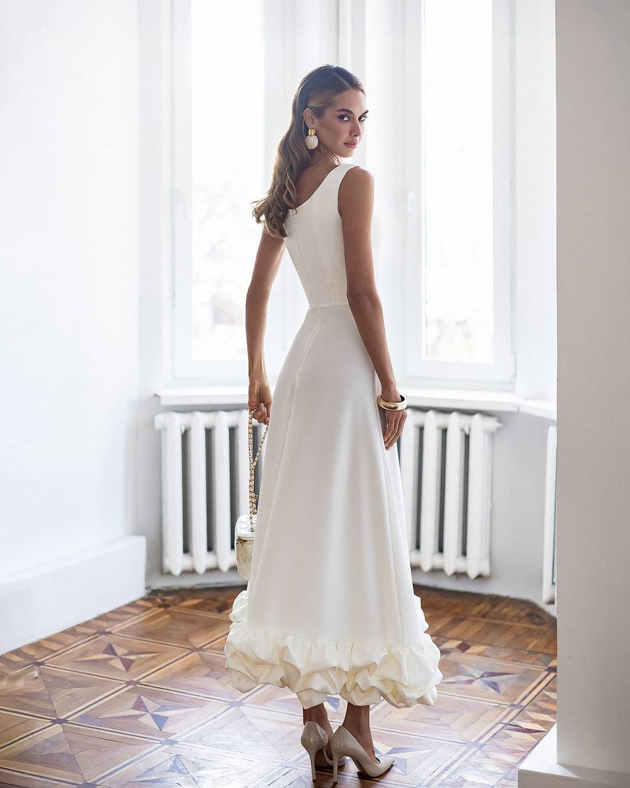 Woman in a white dress standing in a room with large windows and a radiator.