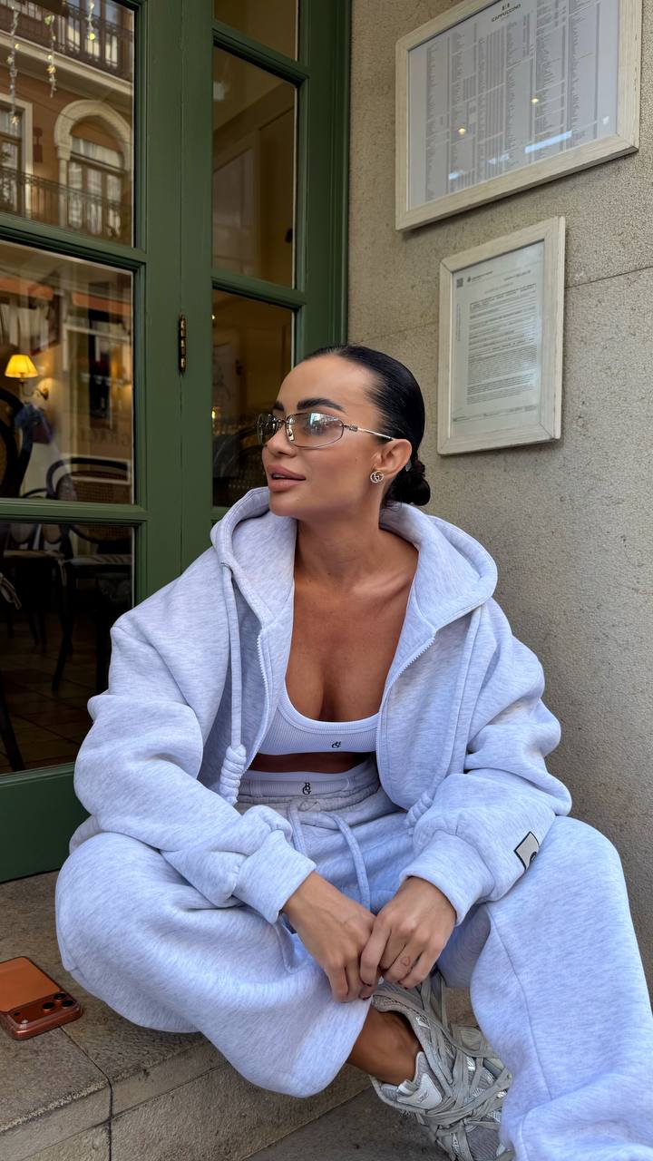 Woman in a light blue tracksuit sitting on a bench outside a building.