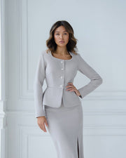 Woman wearing a light gray suit against a white wall