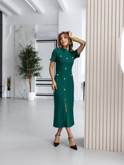 Woman in a green dress posing in a modern indoor setting with plants and white walls.