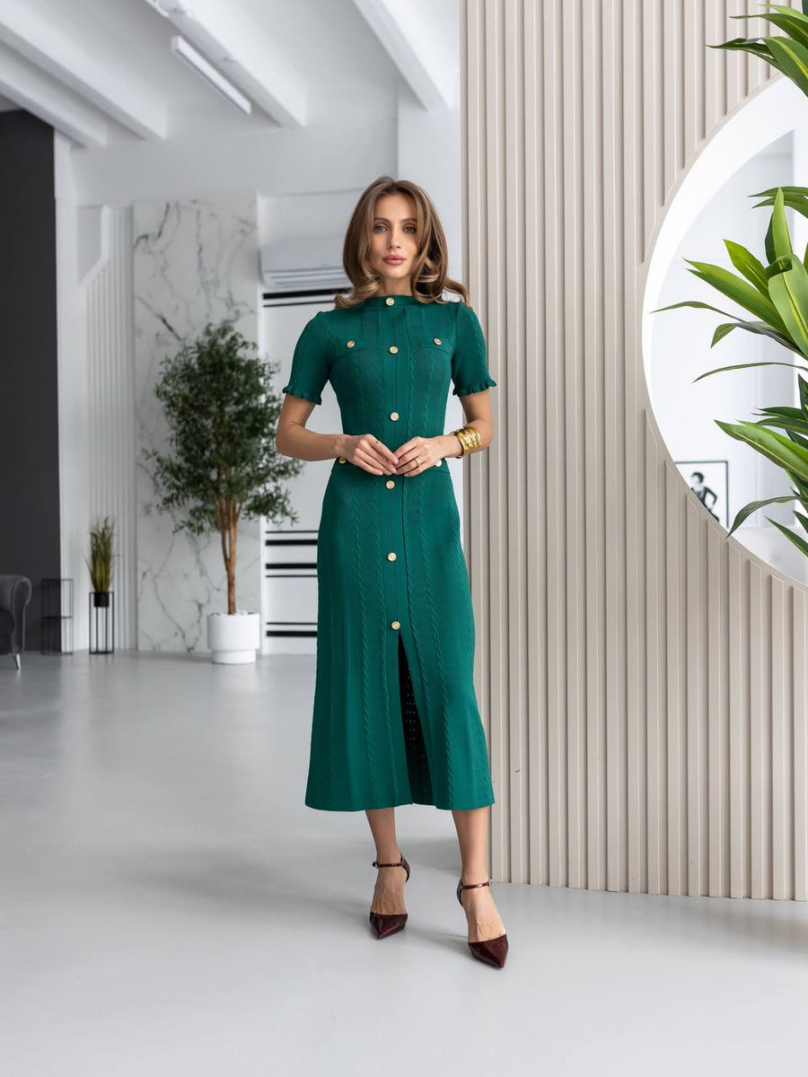 Woman in a green dress standing in a modern indoor setting with plants.