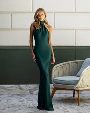 Woman in a green evening gown standing in a stylish room with a chair and decorative wall.