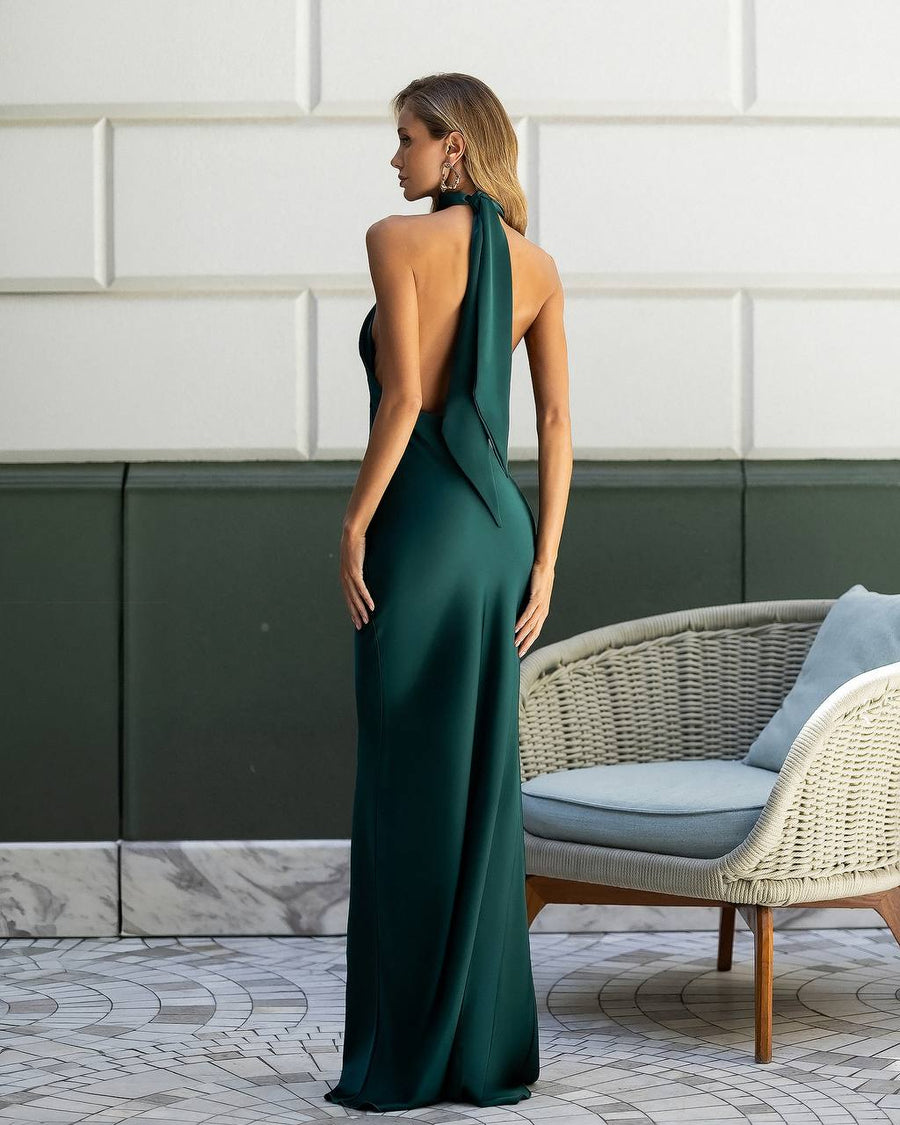 Woman in a green evening gown standing in an outdoor setting with a wicker chair and cushions.