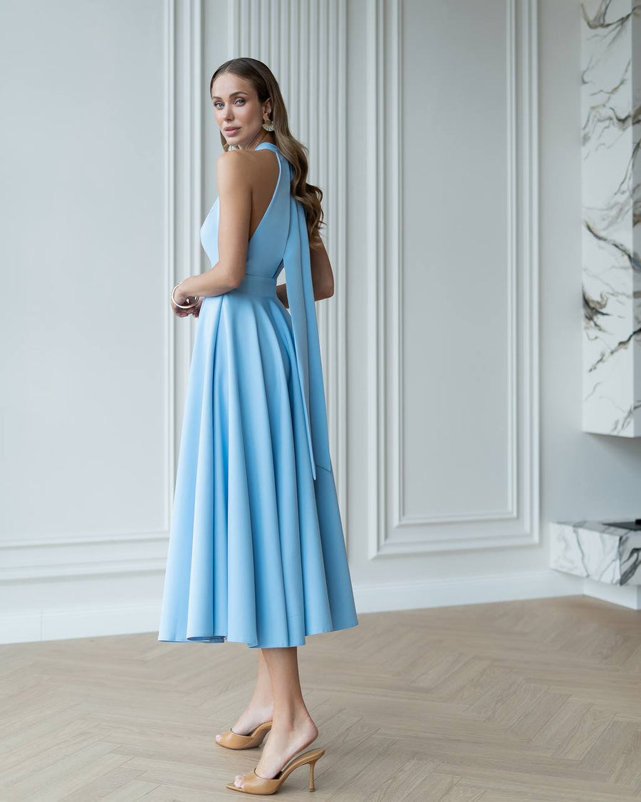 Woman in a light blue dress standing in a room with white walls and a marble column.