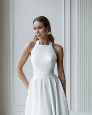 Woman wearing a white halter neck dress against a light gray wall.