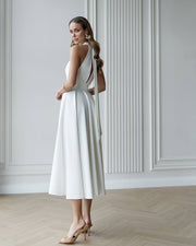 Woman wearing a white dress with cut-out design in a minimalistic room.