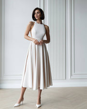 Woman wearing a white dress with a beige skirt against a white wall.
