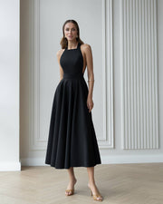 Woman wearing a black dress standing in a room with white walls and wooden floor.