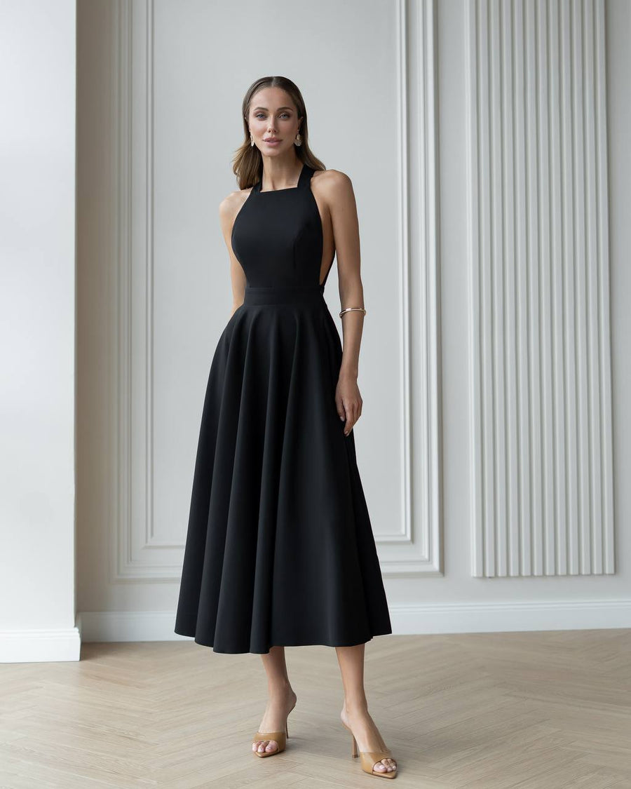 Woman wearing a black dress standing in a room with white walls and wooden floor.