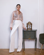 Woman in a pink blouse and white pants standing next to a small table with decorative items.
