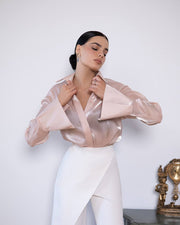 Woman wearing a sheer pink blouse over a white outfit with a decorative clock in the background.