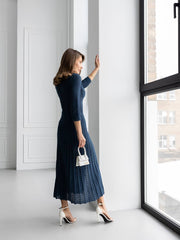 Woman in a blue dress standing by a window in a bright room
