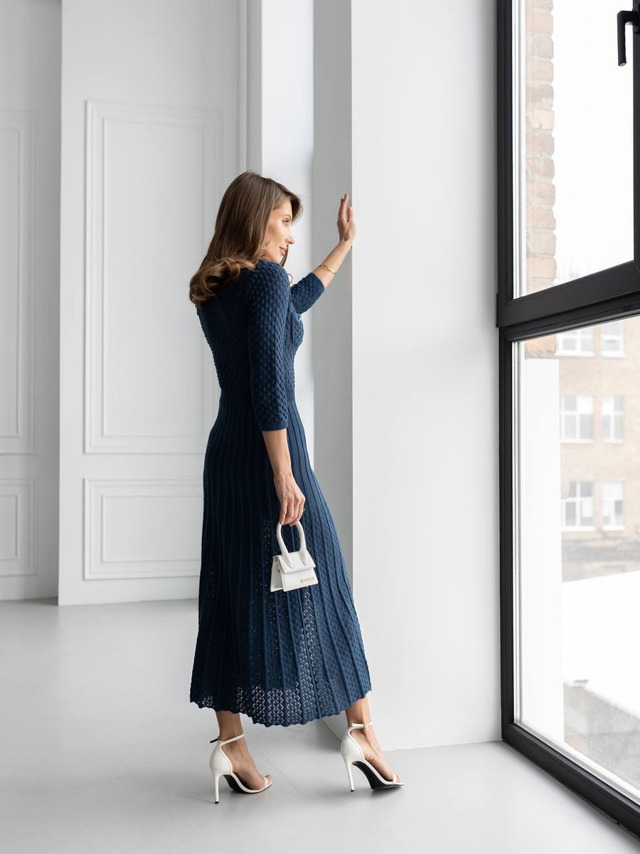 Woman in a blue dress standing by a window in a bright room