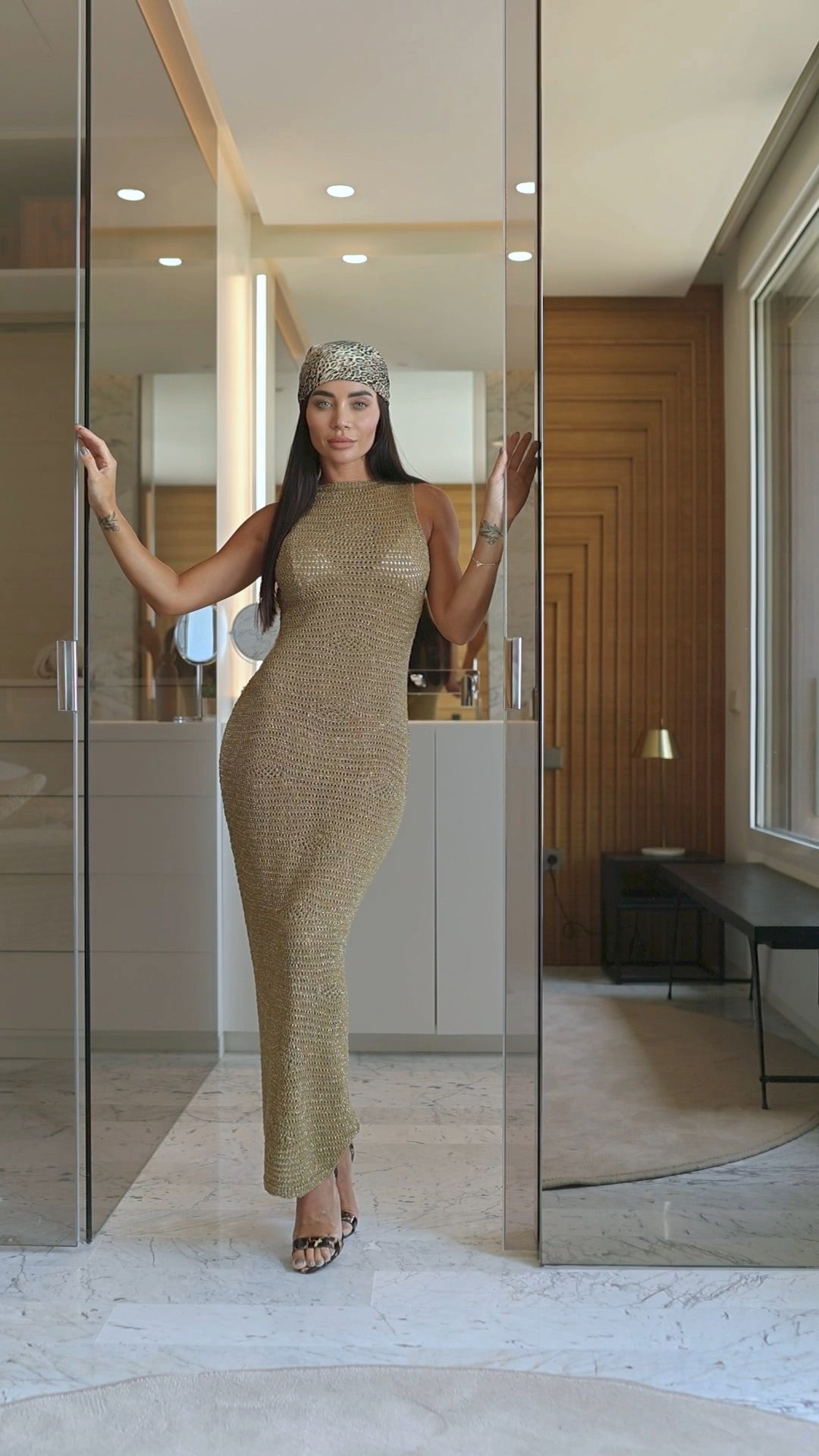 Woman in a gold dress standing in front of a mirror in an indoor setting.