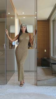 Woman in a gold dress standing in front of a mirror in an indoor setting.