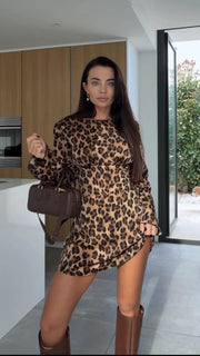 Woman wearing a leopard print dress with brown boots and handbag in a modern kitchen.