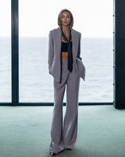 Woman in a gray suit standing in front of large windows with a blurred background