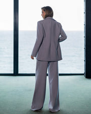 Person wearing a light gray suit standing in front of large windows with a snowy landscape outside.