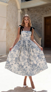 Woman wearing a blue floral dress with black accents in an outdoor setting.