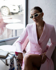 Woman in a pink outfit sitting indoors wearing sunglasses.