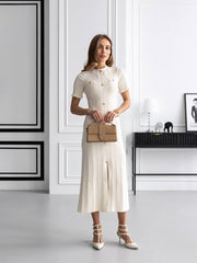 Woman in a white dress holding a brown handbag in a minimalistic room.