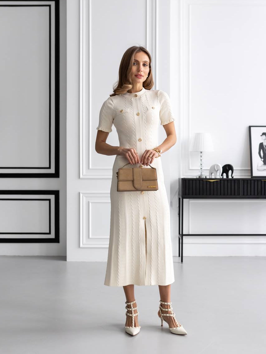Woman in a white dress holding a brown handbag in a minimalistic room.