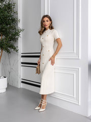 Woman in a white dress standing in a modern interior setting with a plant and decorative wall.