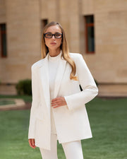 Woman in a white suit standing outdoors with a neutral background